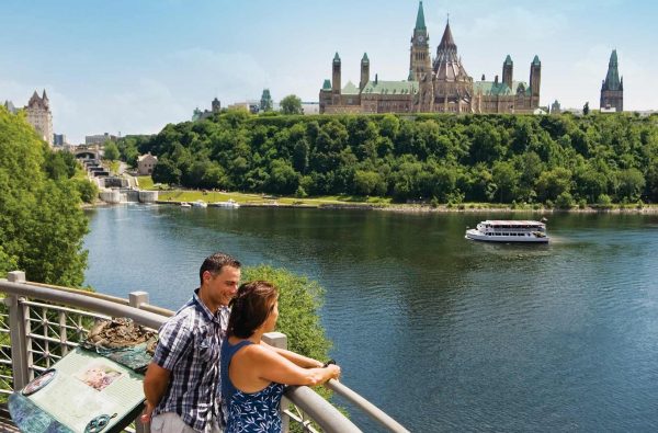 A young couple are looking over the water accross from the Ottawa Parliament building.