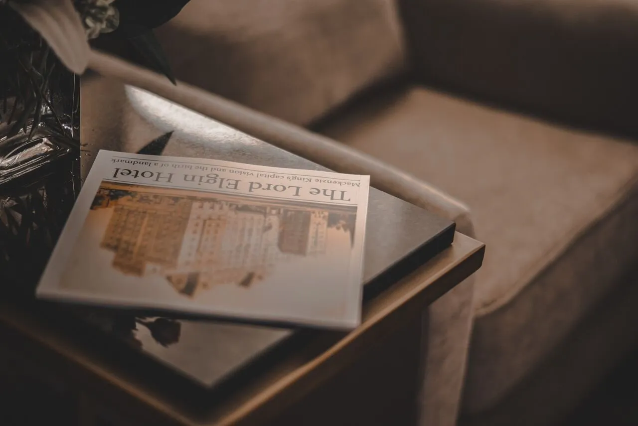 Image of newspaper featuring the Lord Elgin Hotel on a black coffee table beside a chair.