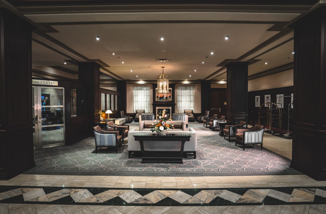 The lobby of the Lord Elgin Hotel, with brown and black marble floors, striped chairs, and a rectangular gold and glass chandelier hanging from the middle of the ceiling.