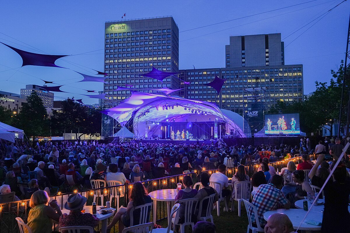 View of the stage at Ottawa's Jazz Festival, with a crowd of people looking towards the band on-stage under purple lighting.