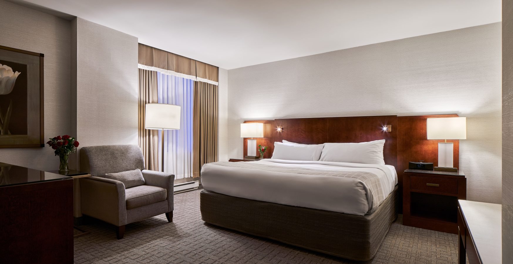 An accessible Lord Elgin Hotel room featuring a large Queen-sized bed, a grey chair and floor to ceiling windows.
