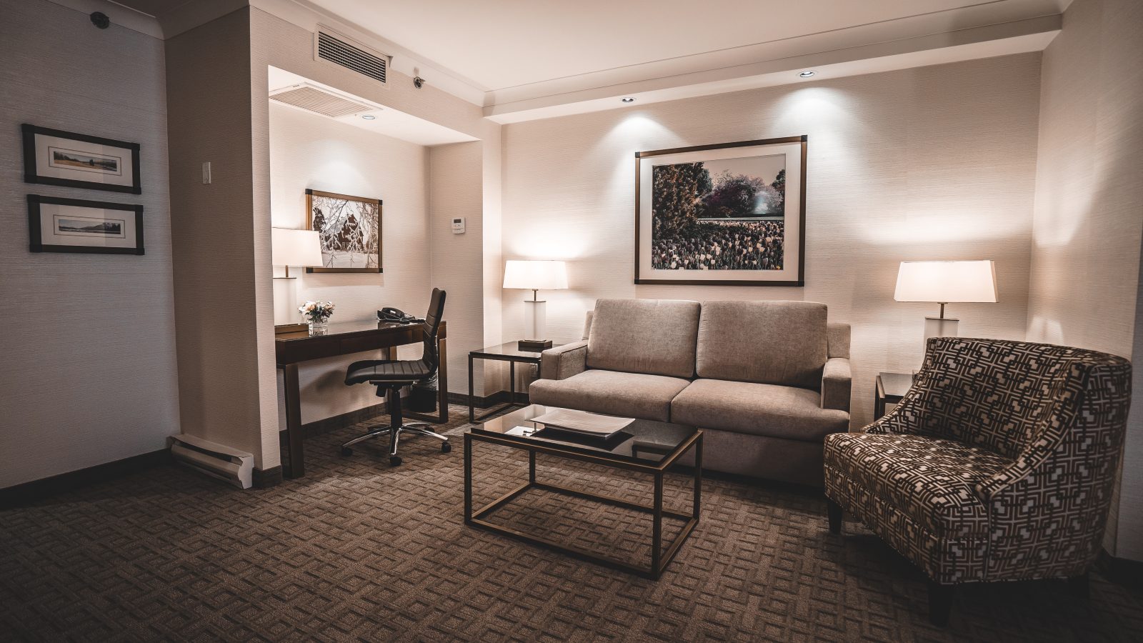 The living room of the Churchill Suite at the Lord Elgin Hotel, featuring a black and gold coffee table, a grey couch, and a wooden desk with a black leather chair.