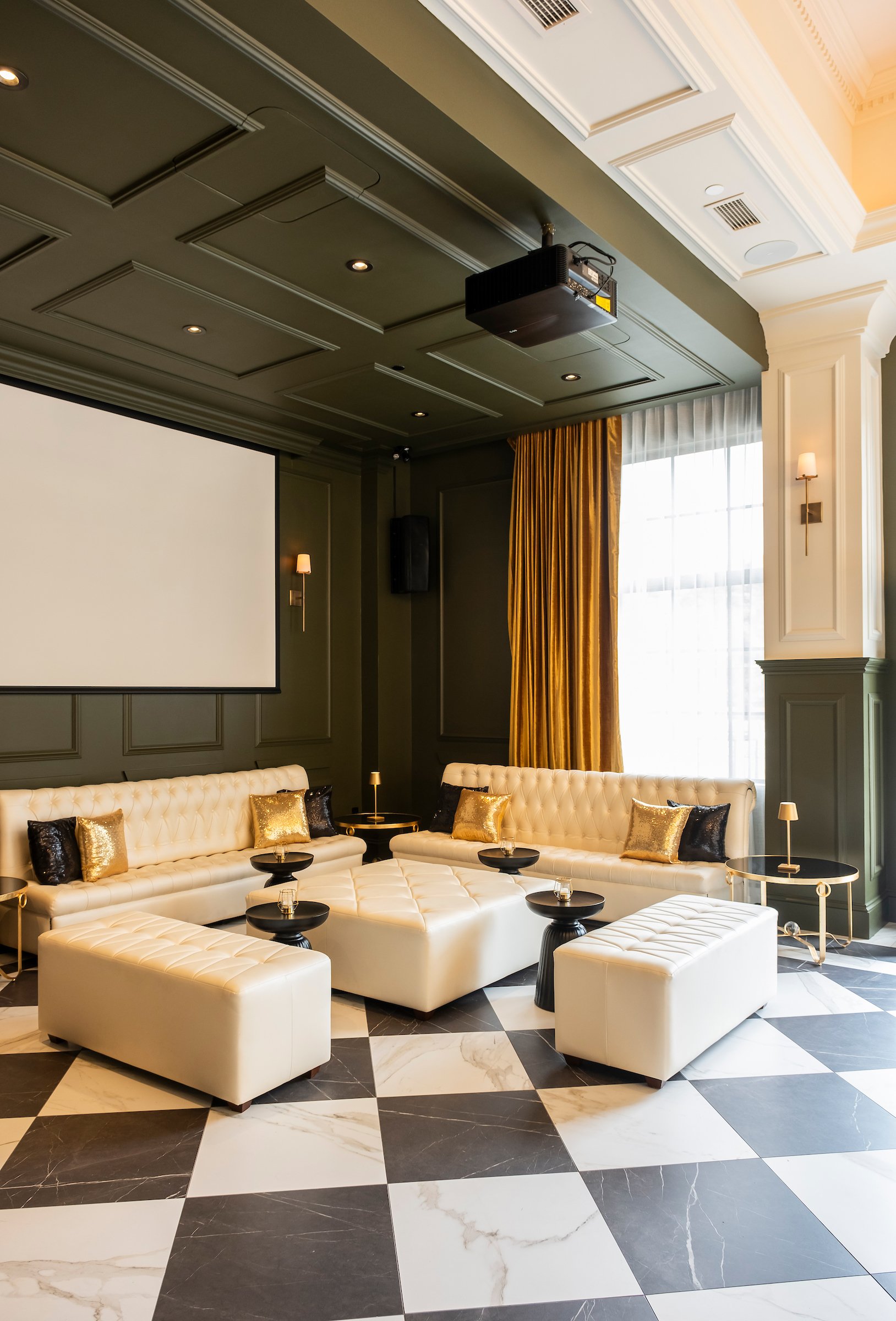 An events space at the Lord Elgin Hotel with black and white checkered marble floors, green and white walls, a projector and white leather furniture.