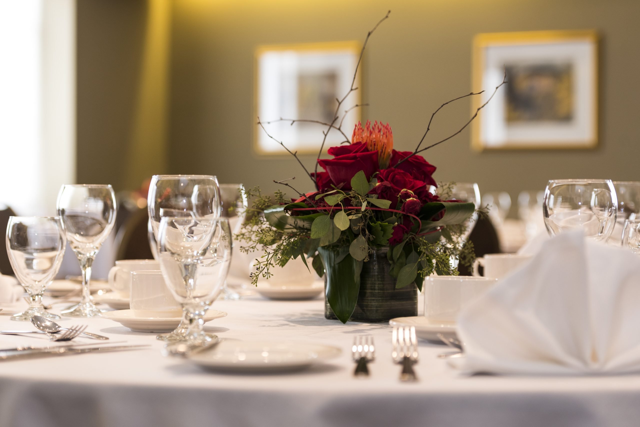 A table with a white tablecloth, glassware, white plates, silverware, and a bouquet of red roses in the middle.