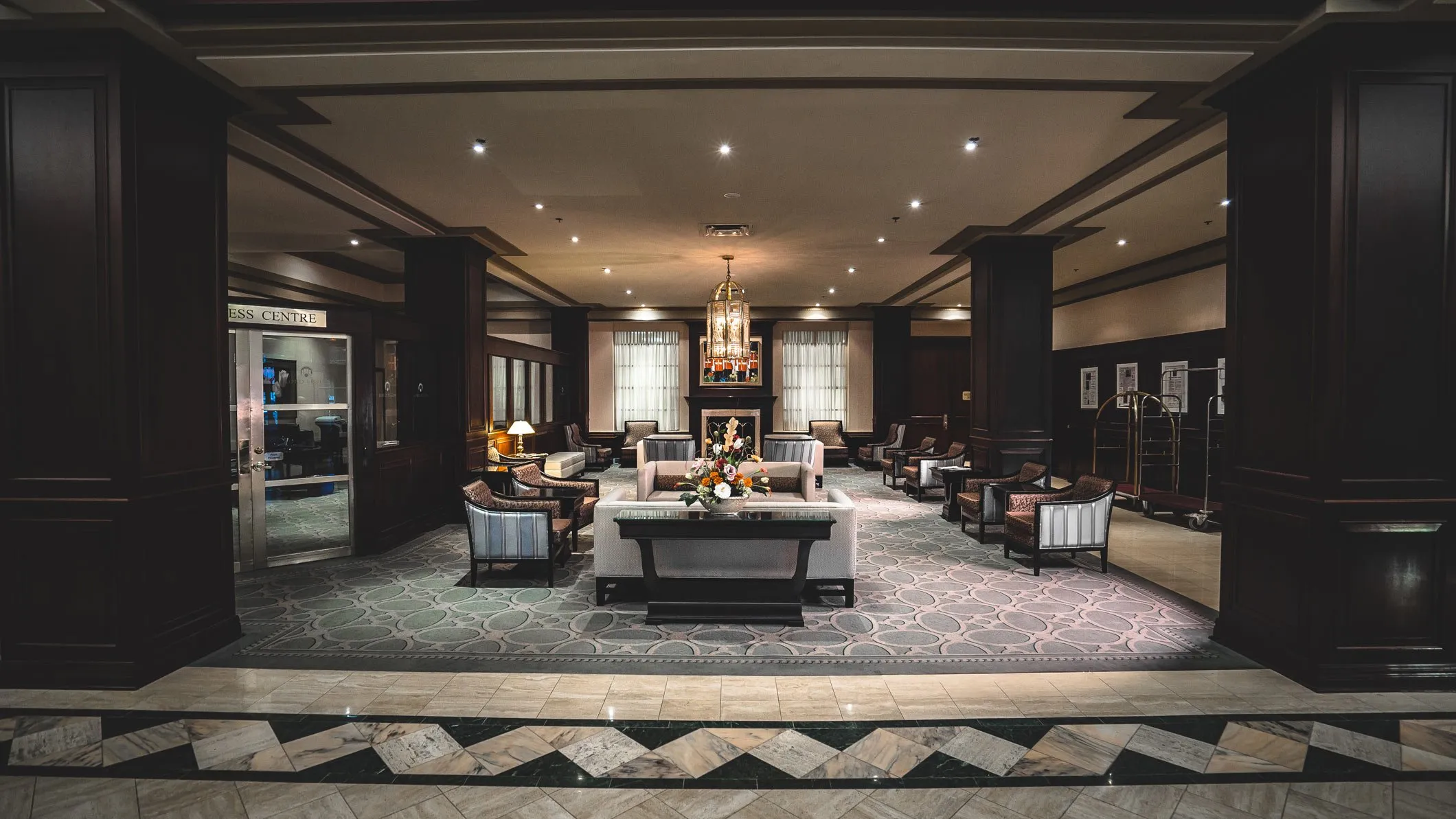 The lobby of the Lord Elgin Hotel, with seating areas, a fireplace, and large chandelier.